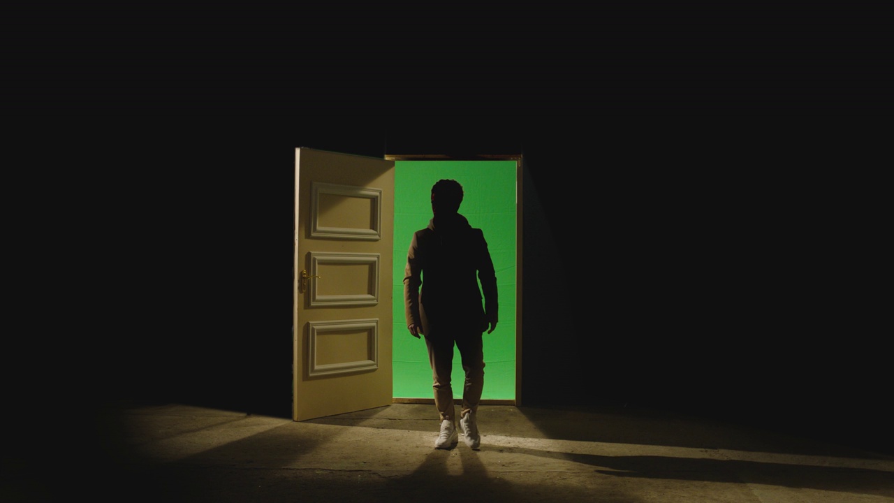 4K前面的观点，一个人走在前面的一扇敞开的门后面的黑暗。商人走在地板附近的绿色屏幕门的镜头。走出困境的方法视频下载