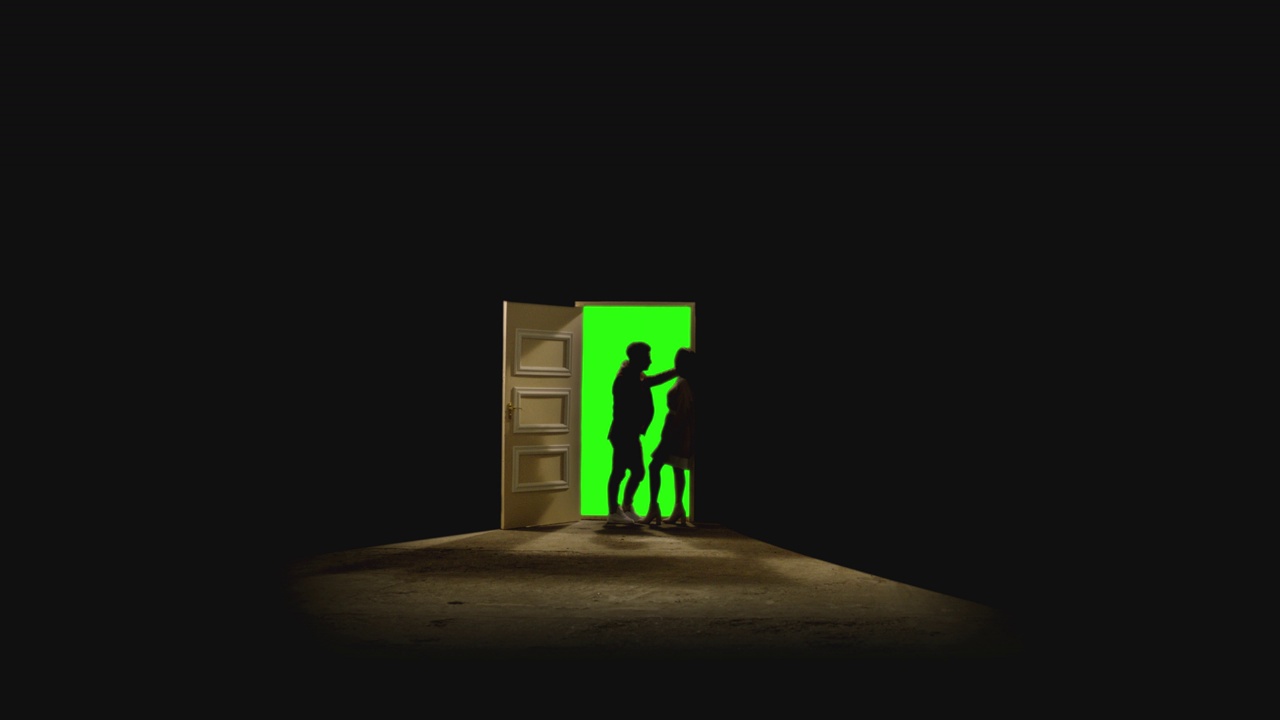 4K侧面视图的夫妇站在对面，看着对方在打开的门前面，后面的黑暗。镜头中，一对夫妇站在带有绿色屏风的门附近的地板上。梦想或浪漫的概念视频素材