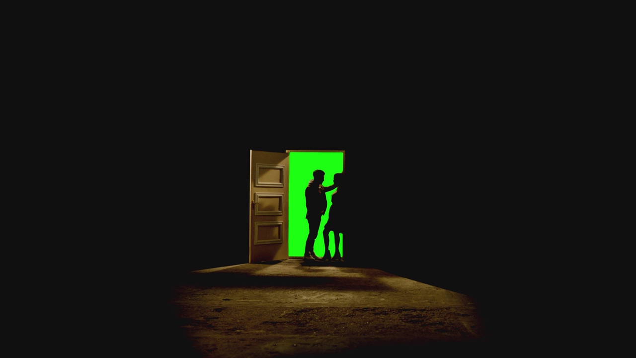 4K侧面视图的夫妇站在对面，看着对方在打开的门前面，后面的黑暗。镜头中，一对夫妇站在带有绿色屏风的门附近的地板上。梦想或浪漫的概念视频素材