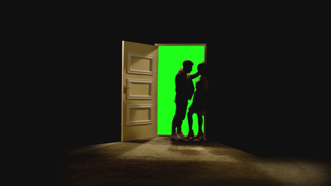 4K侧面视图的夫妇站在对面，看着对方在打开的门前面，后面的黑暗。镜头中，一对夫妇站在带有绿色屏风的门附近的地板上。梦想或浪漫的概念视频下载