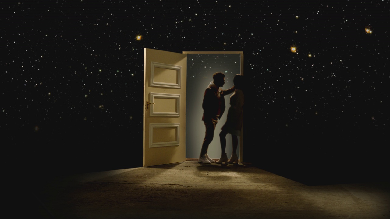 4K侧面视图的夫妇站在对面，看着对方在一扇敞开的门后面的星系。一对情侣站在星星后面的地板上。梦想或浪漫的概念。慢动作视频下载
