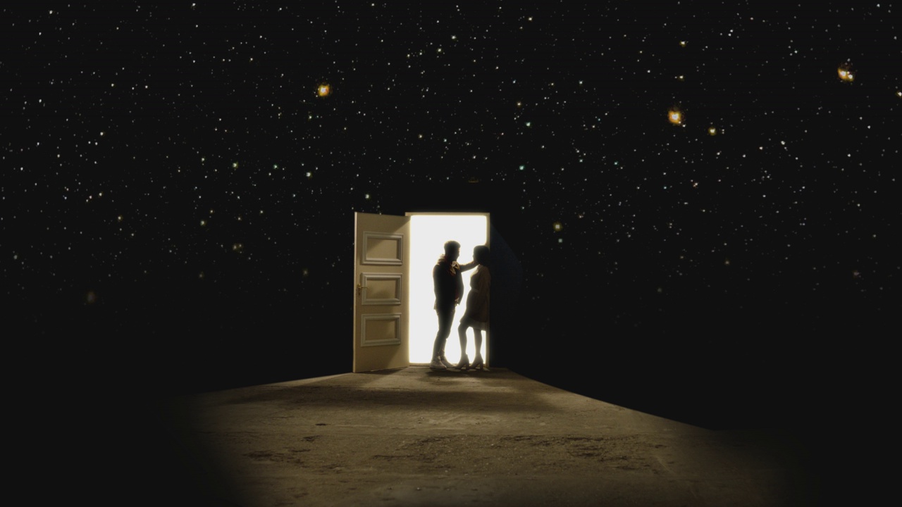 4K侧视图，一对夫妇对面站着，在一扇敞开的门前看着对方，后面有白色的光。一对情侣站在星星后面的地板上。梦幻浪漫的概念。慢动作视频素材