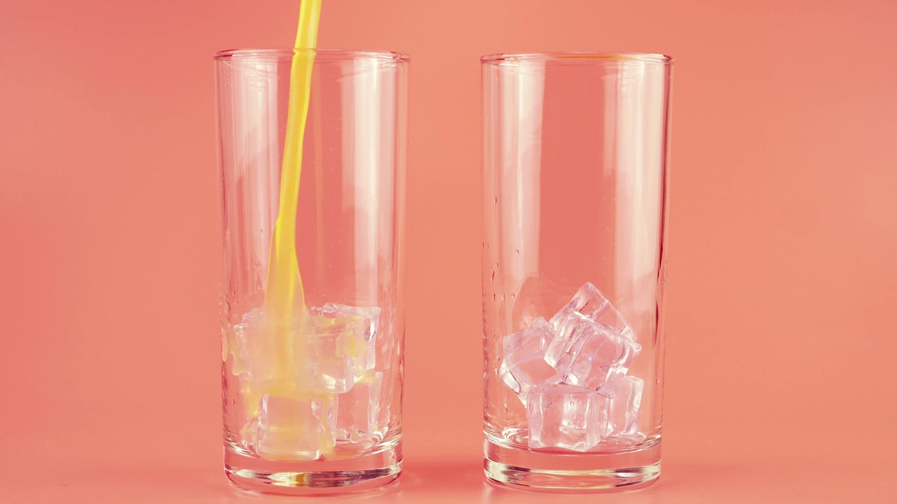 橙汁被倒入玻璃高脚杯，粉色背景上有冰块。缓慢的运动。视频下载