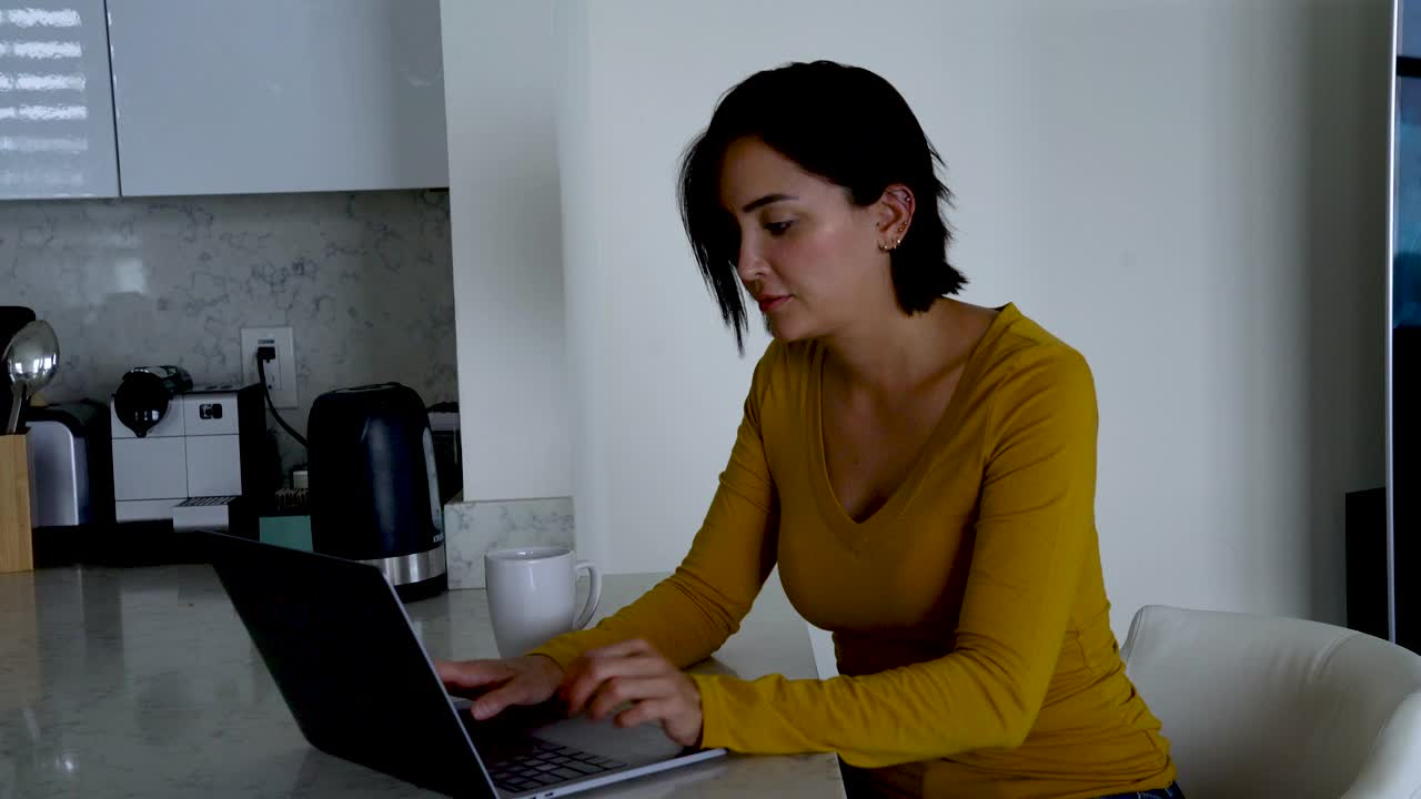 在厨房边喝咖啡边用笔记本电脑工作的女人视频下载