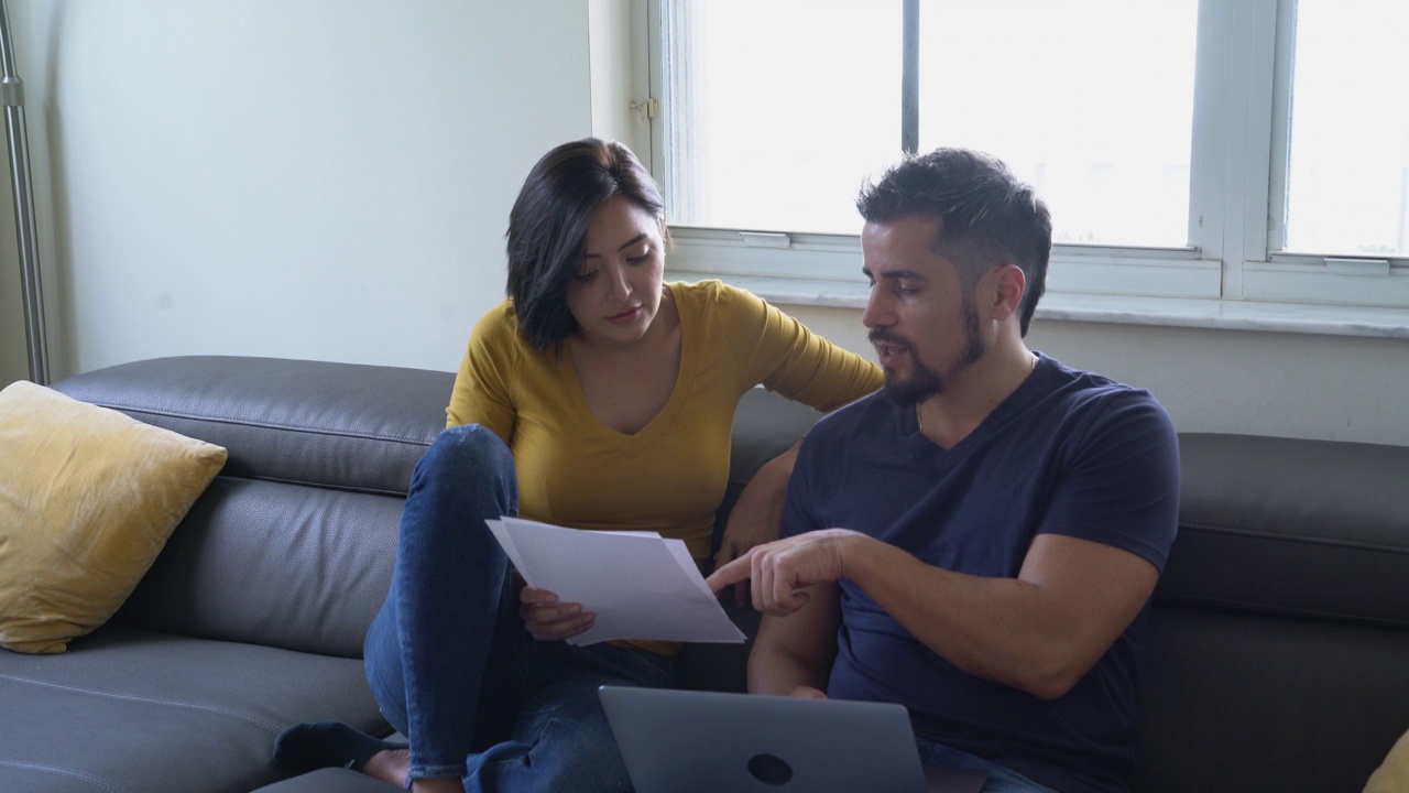 拉丁裔夫妇在客厅的沙发上聊天，检查文件，看笔记本电脑。视频下载