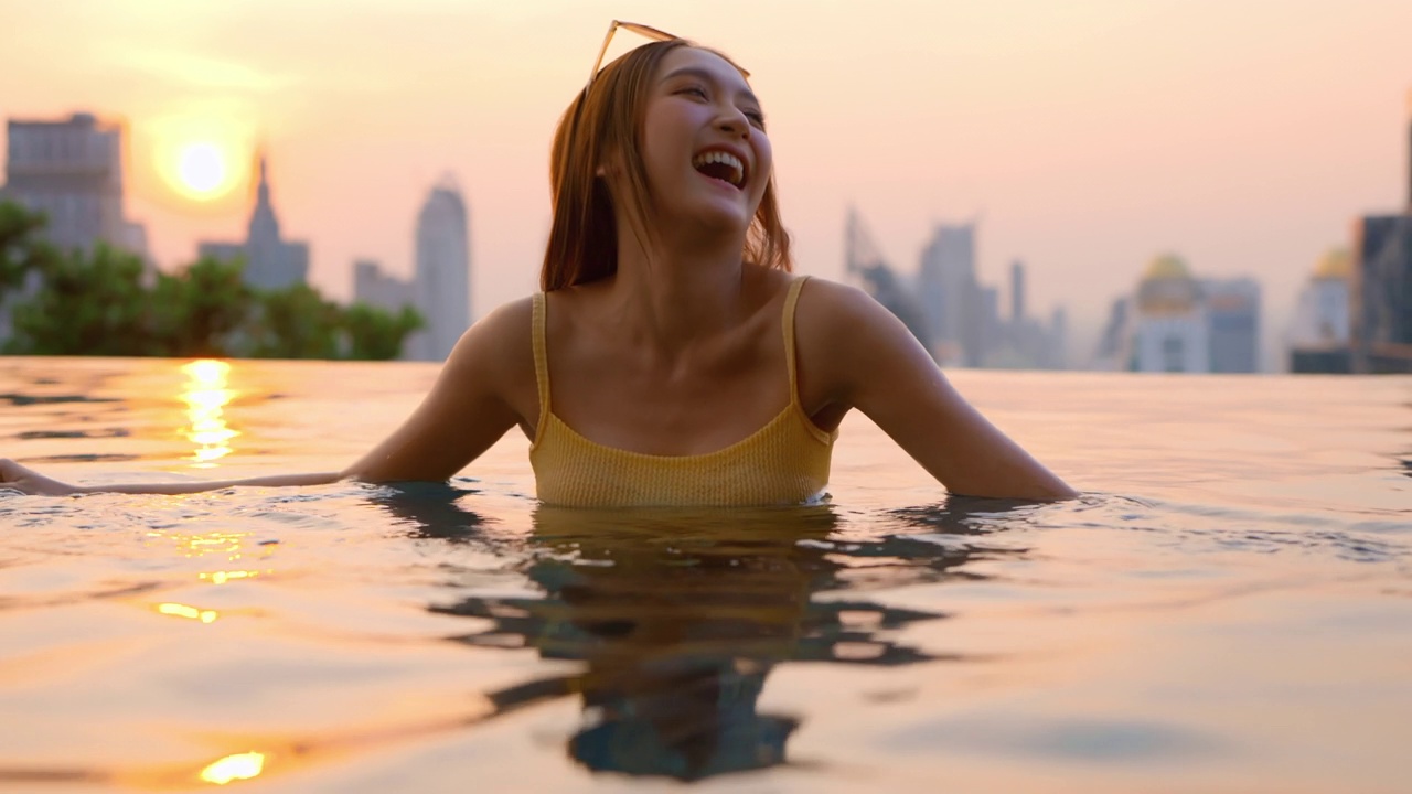 放松夏天休闲休闲亚洲女性女性在泳装上凉爽的藤条泳池长椅上躺在游泳池附近，无边泳池边在建筑物的屋顶上，夏天旅游度假日光浴视频素材