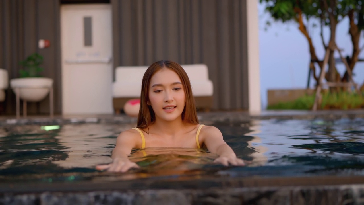 放松夏天休闲休闲亚洲女性女性在泳装上凉爽的藤条泳池长椅上躺在游泳池附近，无边泳池边在建筑物的屋顶上，夏天旅游度假日光浴视频素材