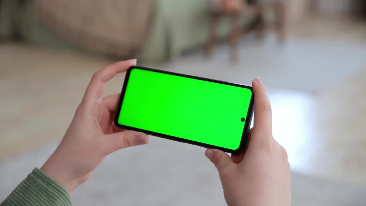 近距离观察女性手使用水平智能手机与关键的绿色屏幕。彩色键模拟流媒体服务的应用程序。在网上看视频。有选择性的重点视频下载