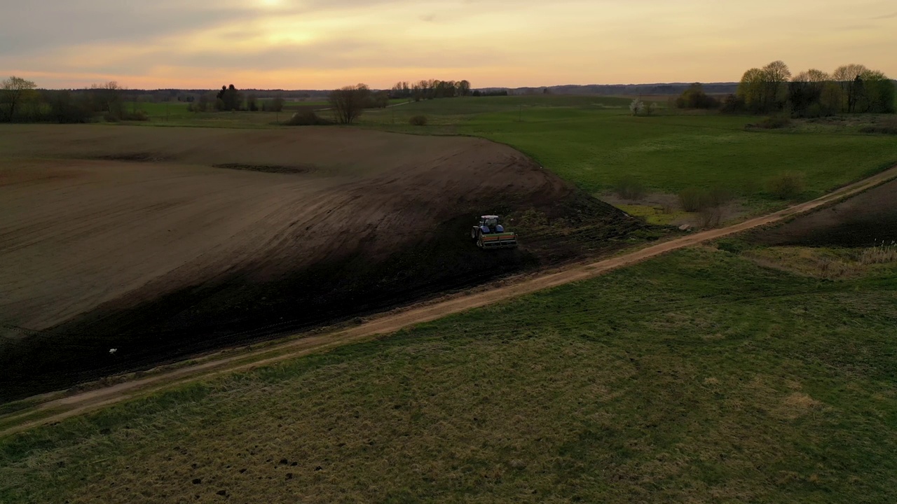 无人机拍摄的农业耕地和农民驾驶拖拉机在春天的黄昏。视频素材