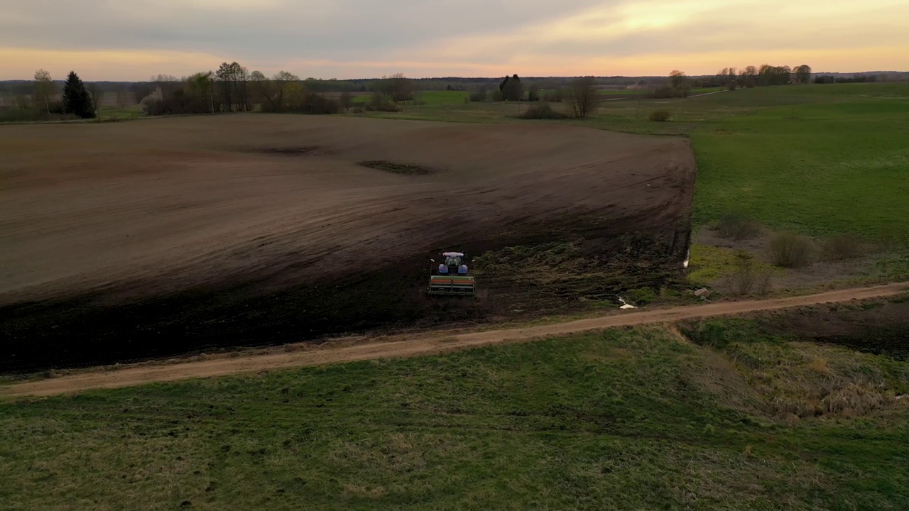 无人机拍摄的农业耕地和农民驾驶拖拉机在春天的黄昏。视频素材