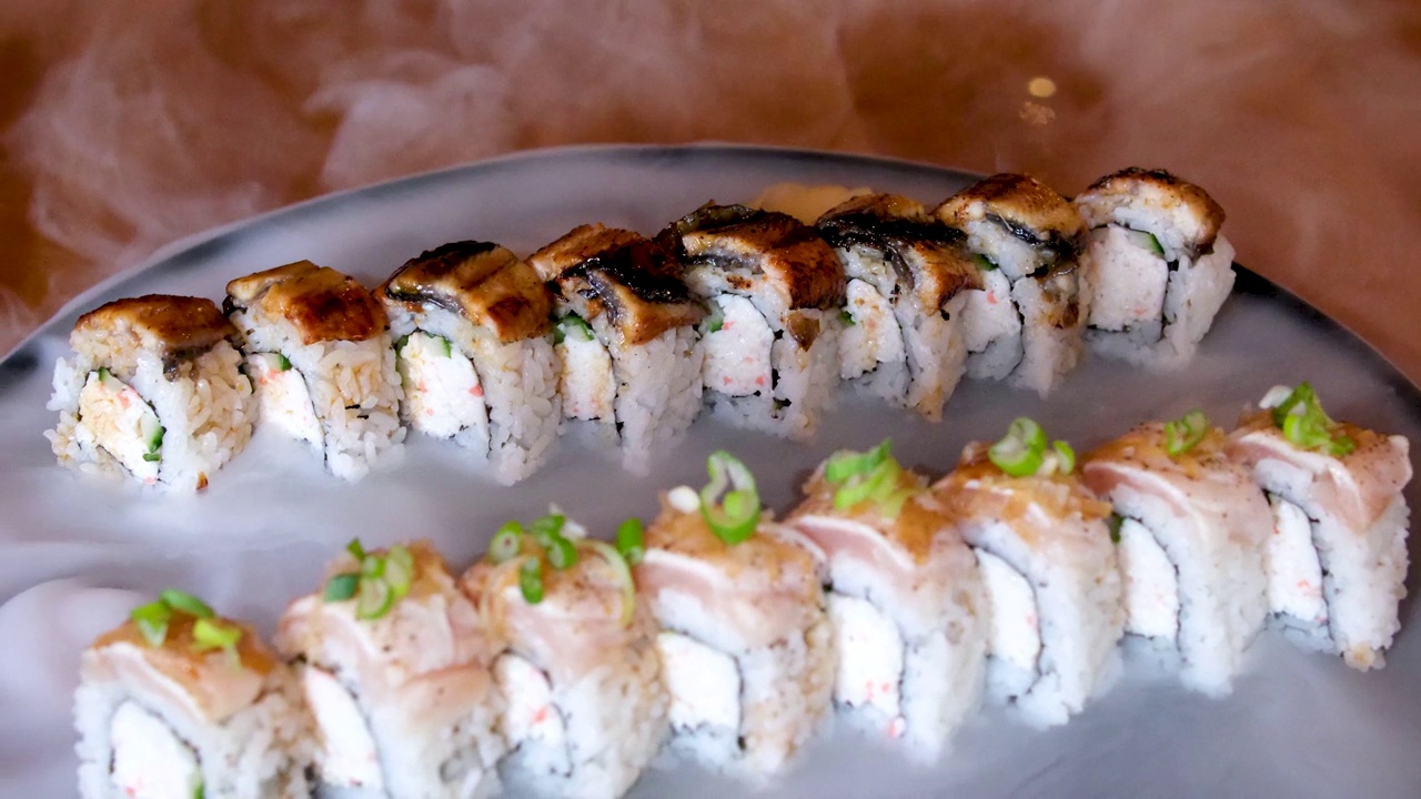 不同种类的寿司卷放在黑色石板上。筷子和酱油碗在旁边。顶角视图。视频下载