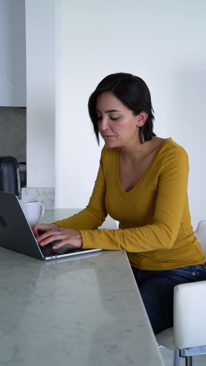 女人一边在厨房喝咖啡，一边愉快地摆弄着笔记本电脑视频下载