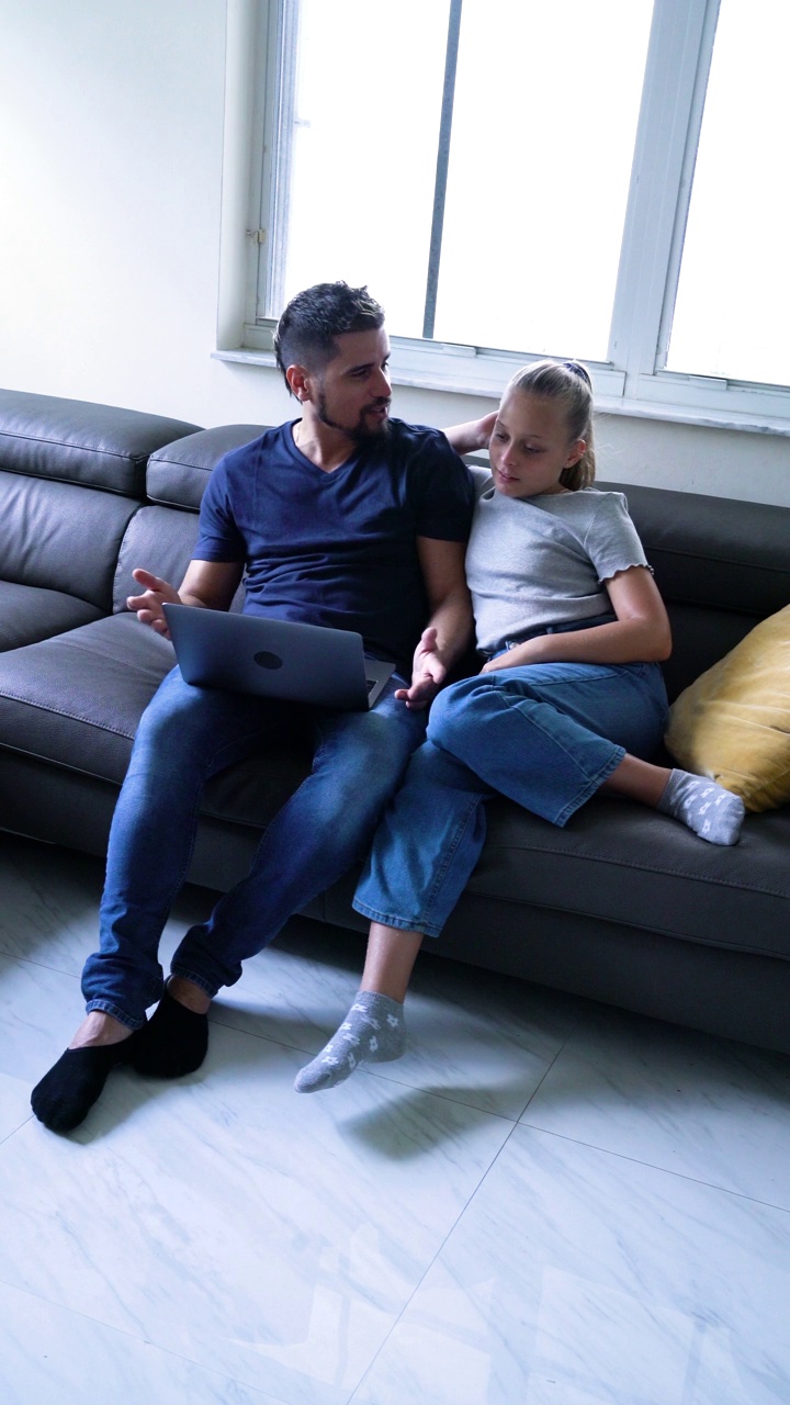 叔叔和侄女在笔记本电脑上看节目，在客厅的沙发上互相拥抱。视频下载