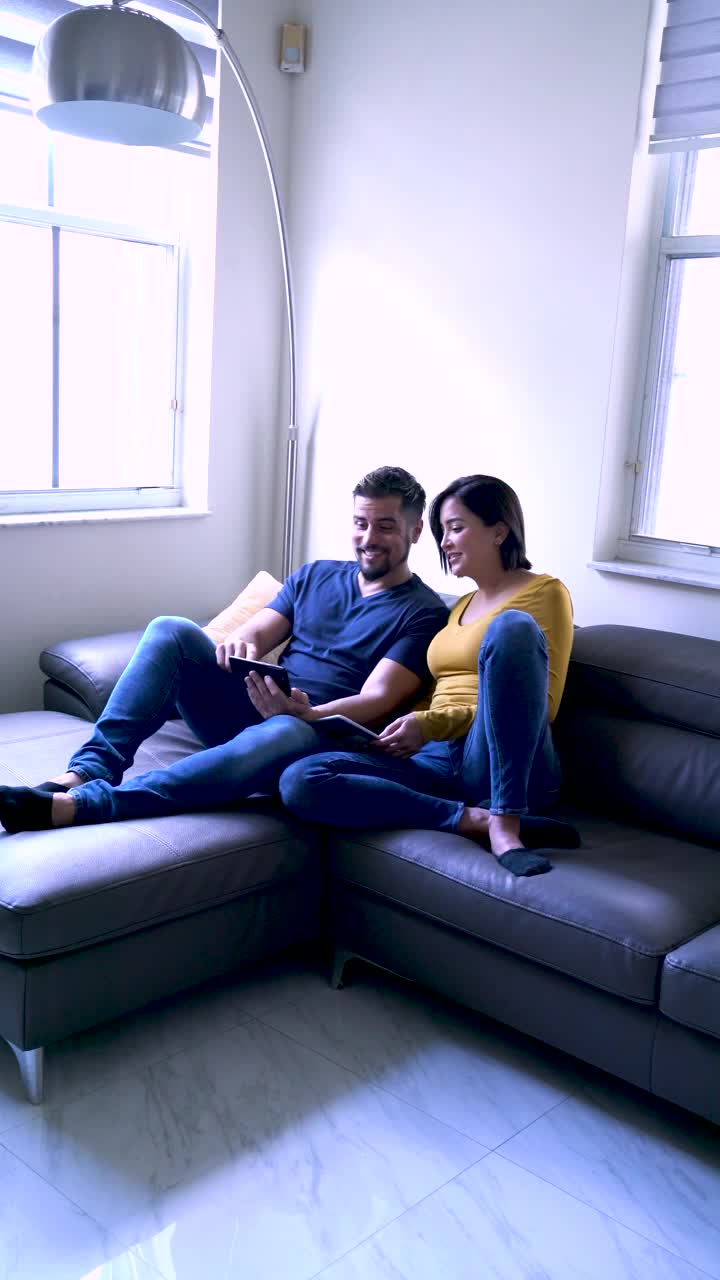 中年拉丁裔夫妇看着设备上有趣的内容，在客厅的沙发上大笑视频下载