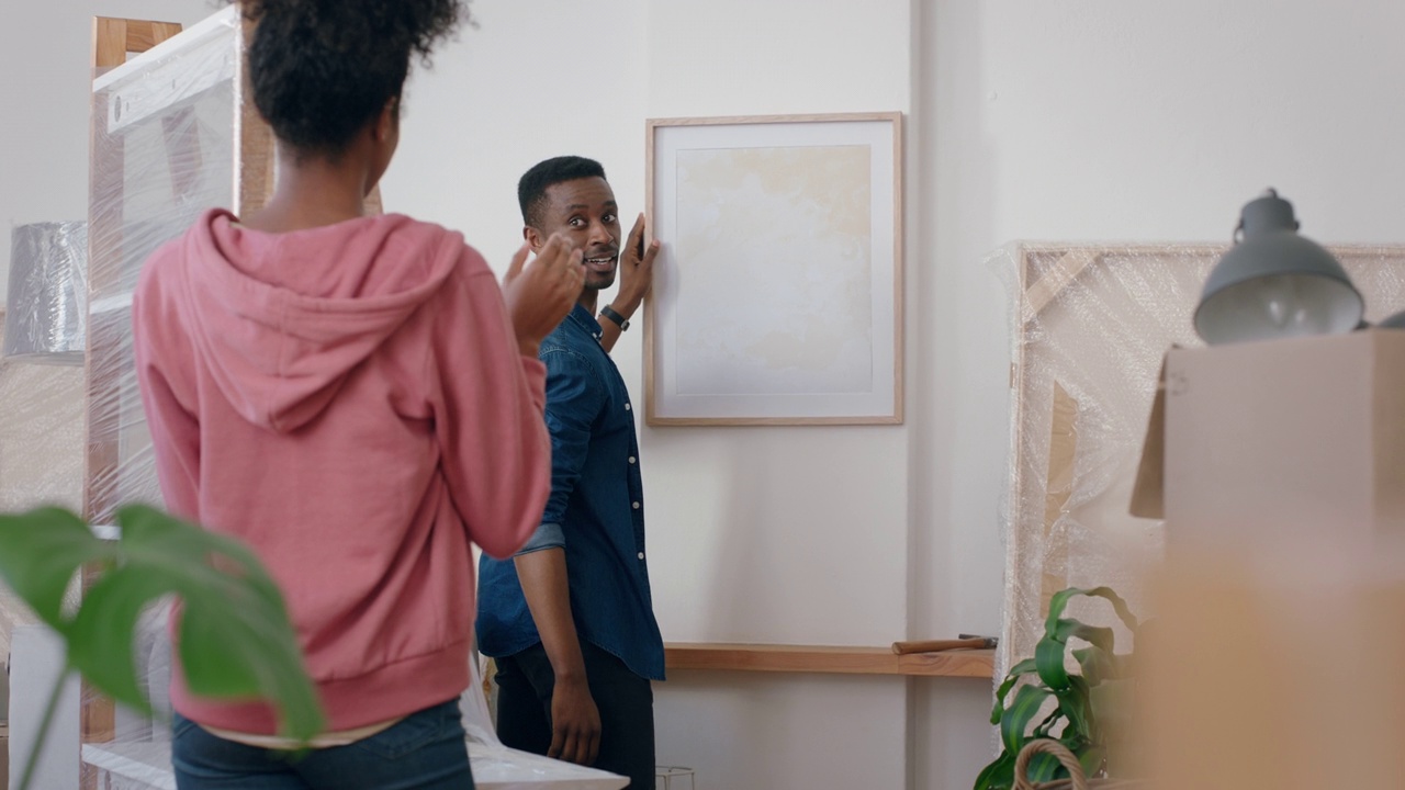 年轻的混血夫妇搬进新房，在墙上挂着照片，一起装饰家，在新公寓享受团队合作的4k镜头视频下载