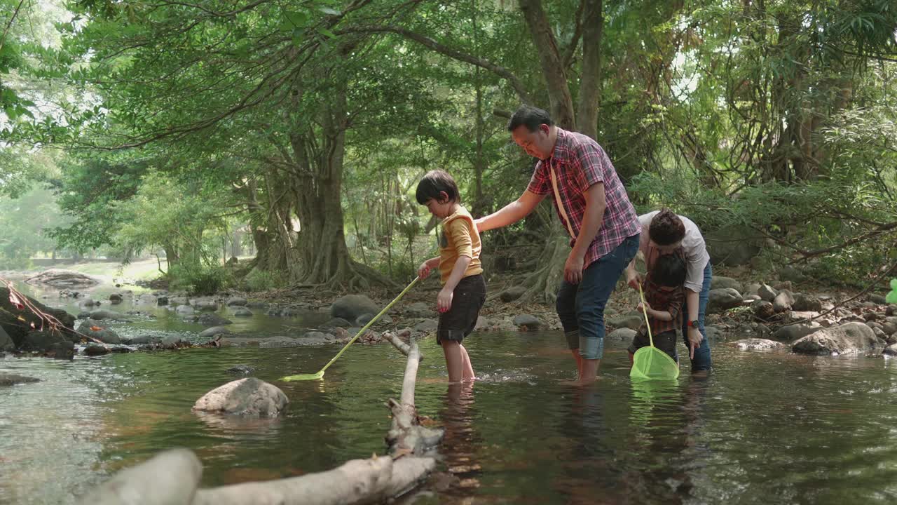 一对年轻的亚洲夫妇和他们漂亮的两岁女儿在外面玩耍，同时给鱼和乌龟喂食。自然主义者家庭的概念。有爱心和快乐的孩子。视频下载