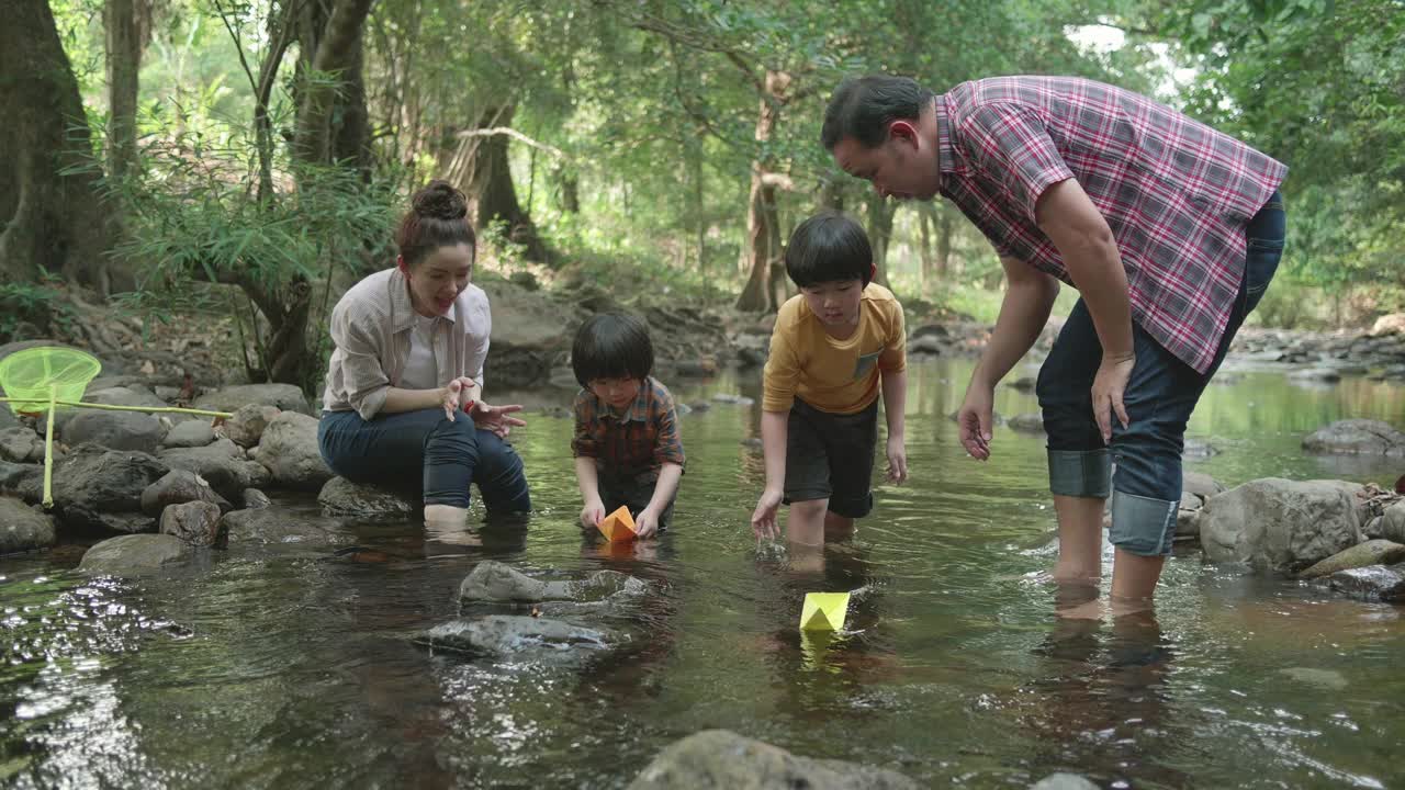 一对年轻的亚洲夫妇和他们漂亮的两岁女儿在外面玩耍，同时给鱼和乌龟喂食。自然主义者家庭的概念。有爱心和快乐的孩子。视频素材