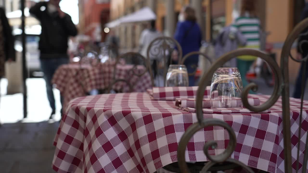欧洲街上的意大利餐厅空桌子上有餐巾和玻璃杯。游客走在后面。Milliken桌布检查点。经典的格子图案视频素材