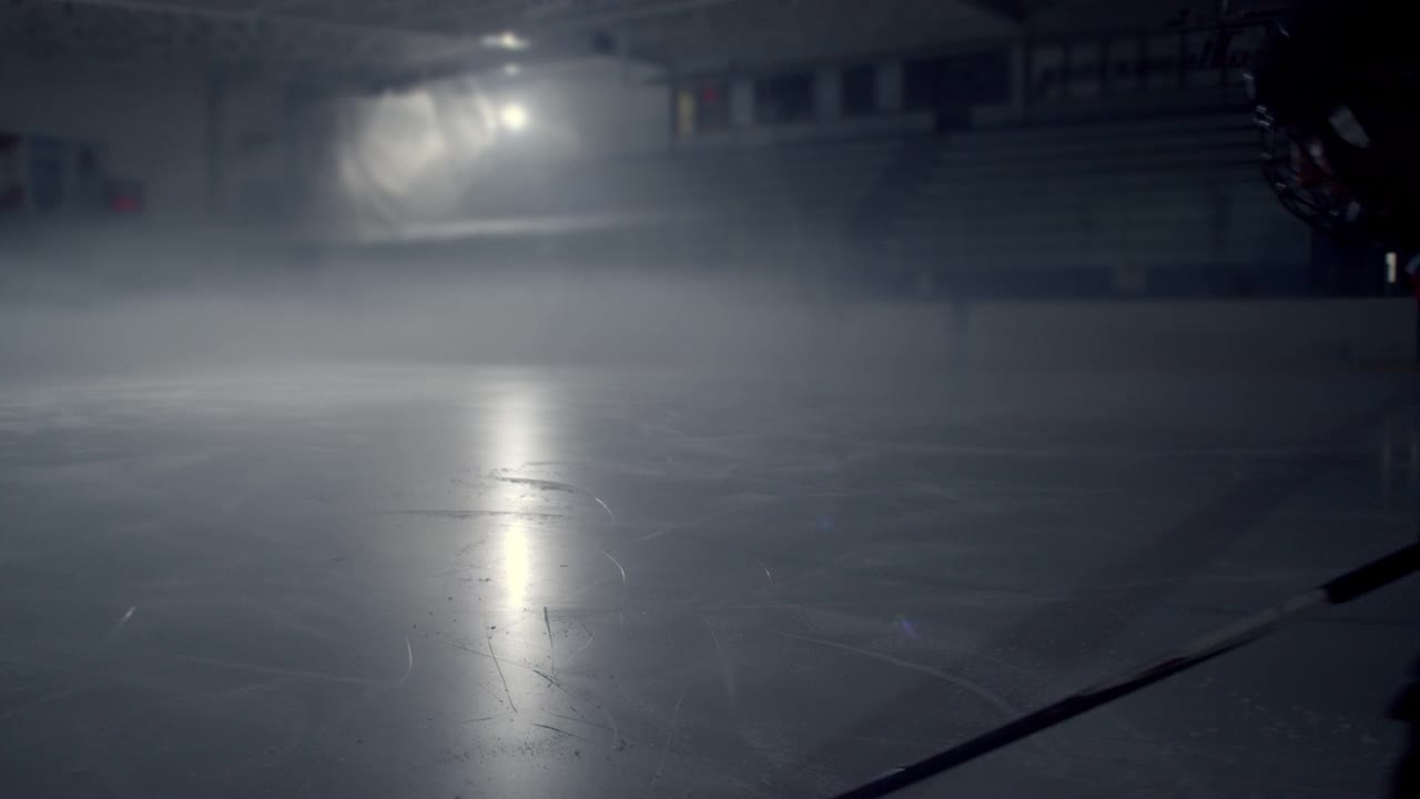 身穿红色制服的冰球运动员踩着冰棍在黑暗中摆弄冰球视频素材
