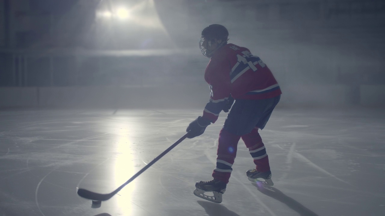 身穿红色制服的冰球运动员踩着冰棍在黑暗中摆弄冰球视频素材