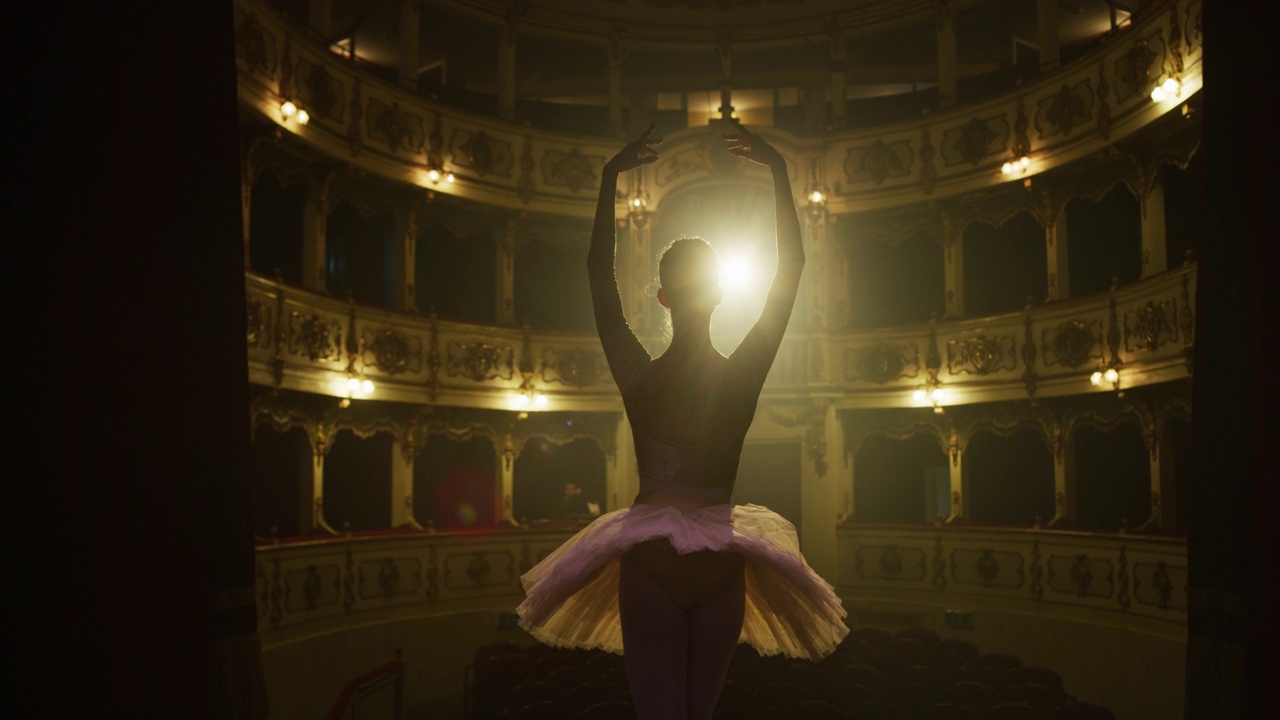 年轻的古典芭蕾舞女演员站在古典剧院舞台上，在聚光灯下谢幕。优雅的表演者接受观众对她才华的掌声视频下载