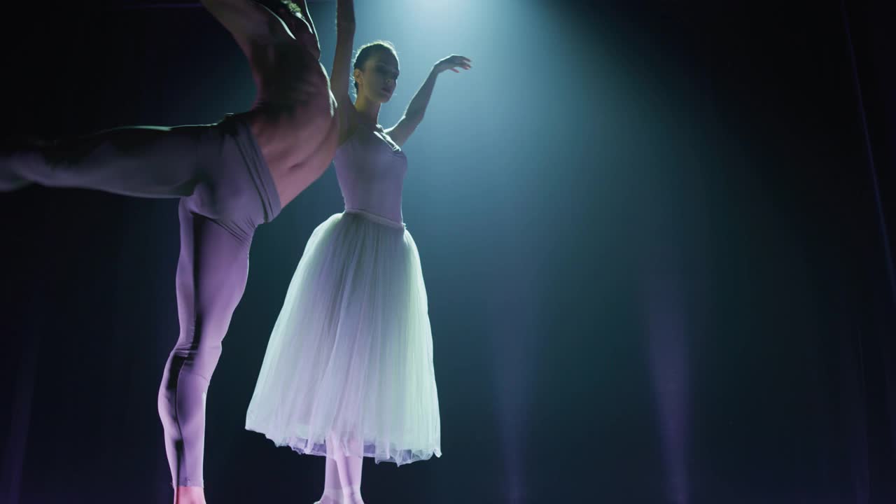 两个年轻的古典芭蕾舞演员在戏剧舞台上用戏剧灯光表演的电影镜头。专业的男女演员在表演前一起排练他们的舞蹈视频下载