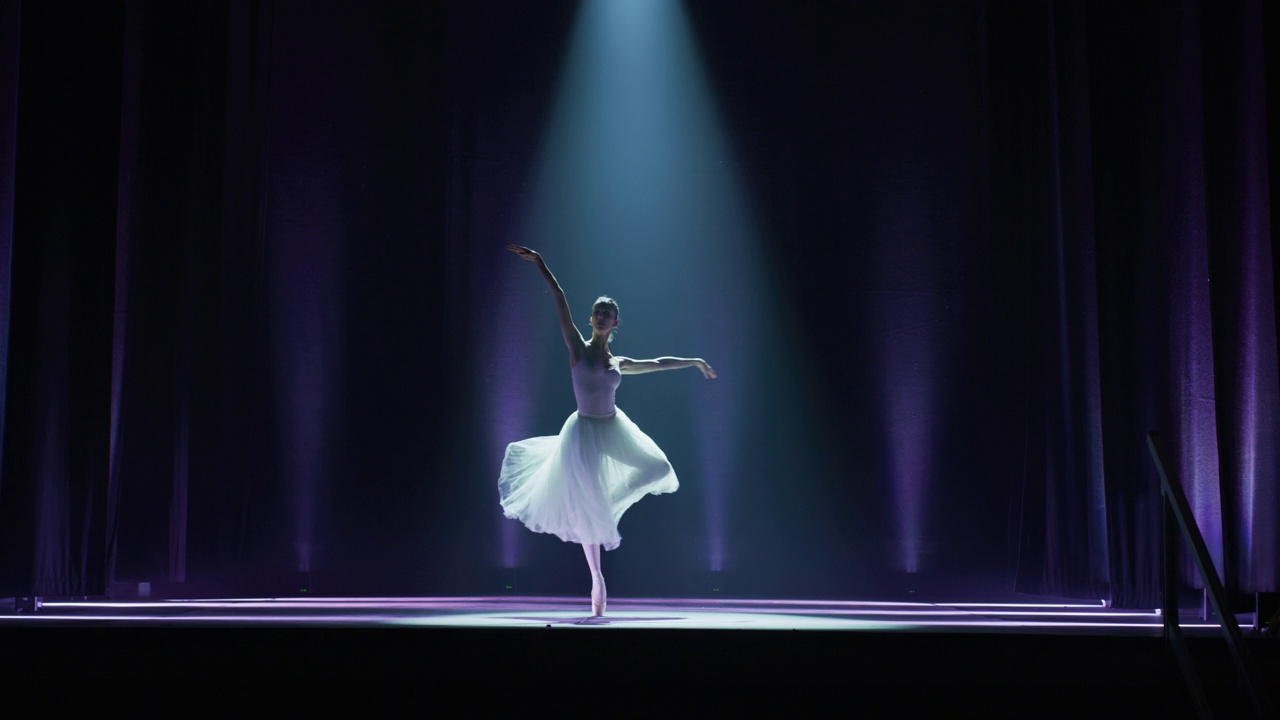 年轻优雅的古典芭蕾舞女舞者在戏剧舞台上表演的广角镜头与戏剧性的聚光灯照明。穿着白色芭蕾舞裙的女人正在为演出排练舞蹈视频下载