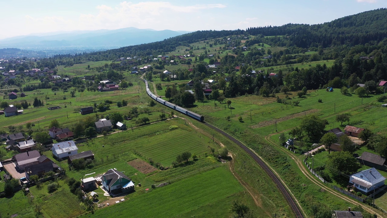 火车在喀尔巴阡山脉的铁轨上行驶，穿过村庄鸟瞰图视频下载