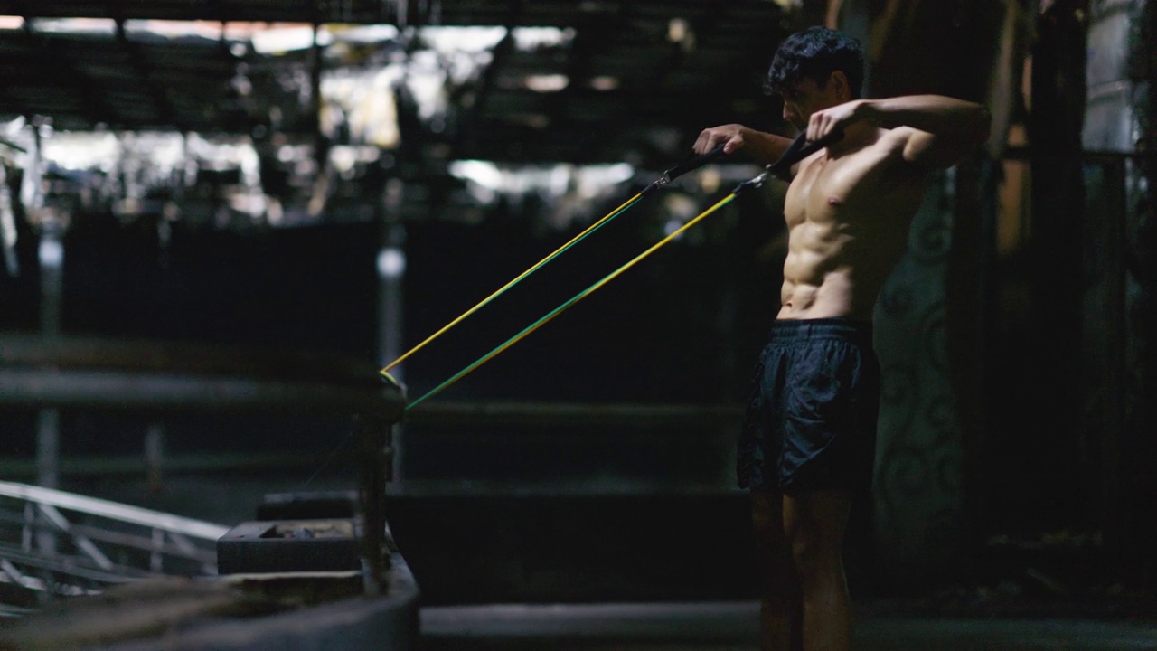 肌肉发达的男人在黑暗的阳光下在健身房锻炼。视频下载
