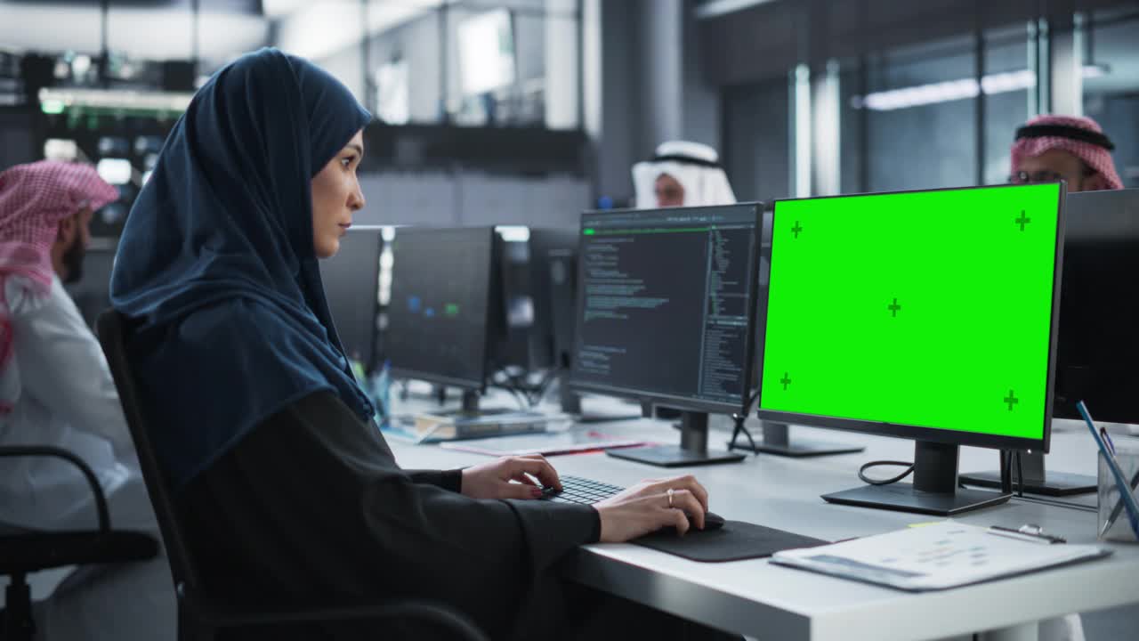 阿拉伯女性软件开发人员工作在台式电脑与绿屏模拟显示。年轻的中东专家测试创新金融科技项目的编程代码视频下载