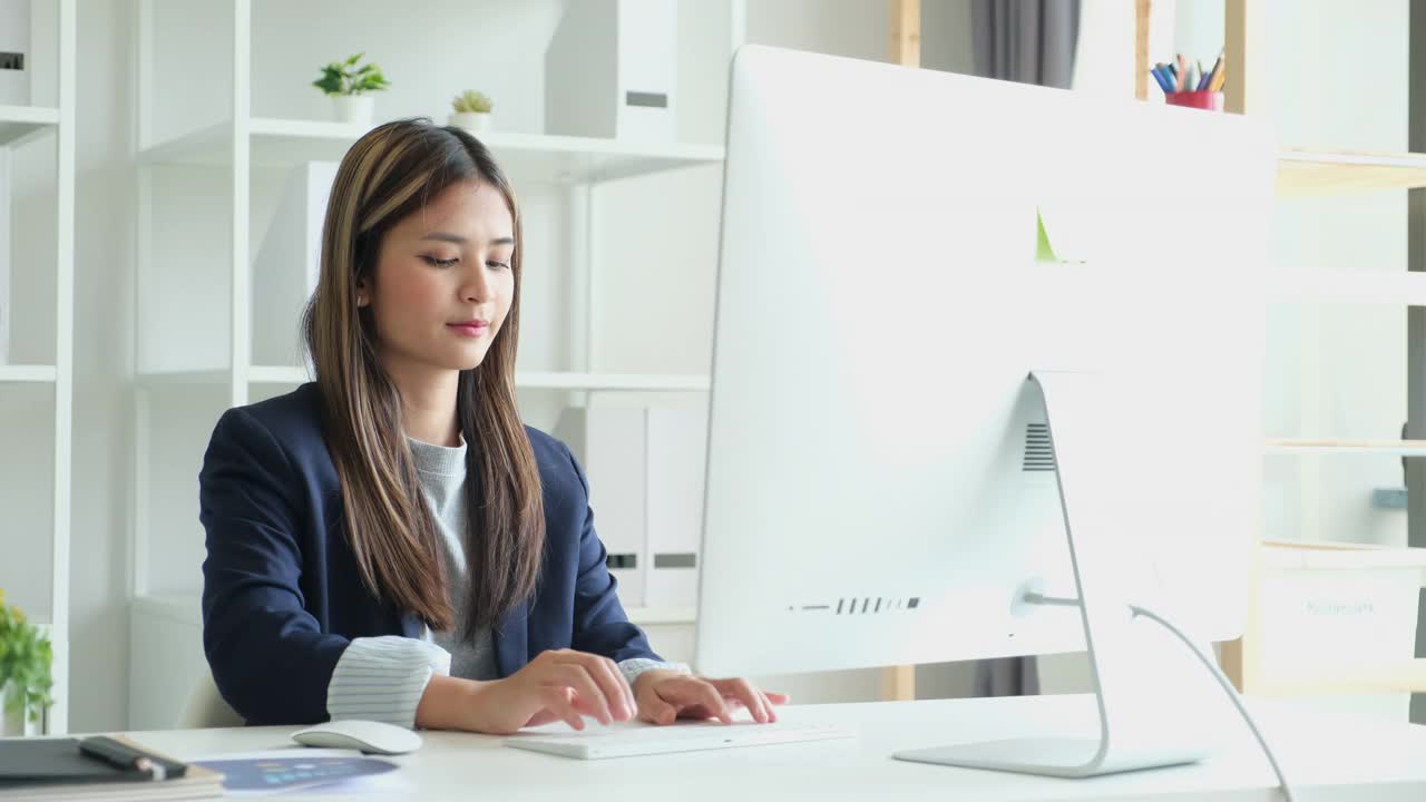 年轻的亚洲妇女使用台式电脑，而坐在家里办公室视频素材