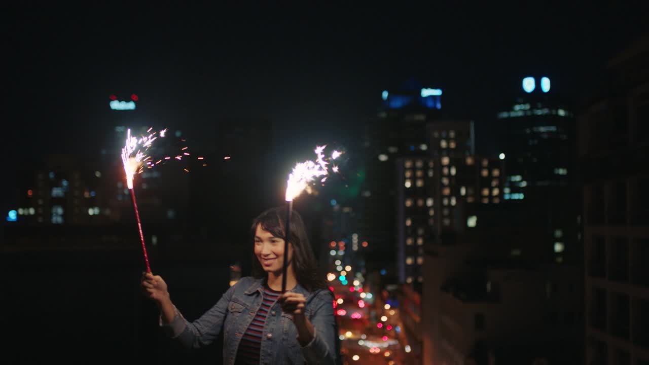 快乐的年轻女子拿着烟花跳舞在屋顶上庆祝除夕享受节日庆祝活动视频素材