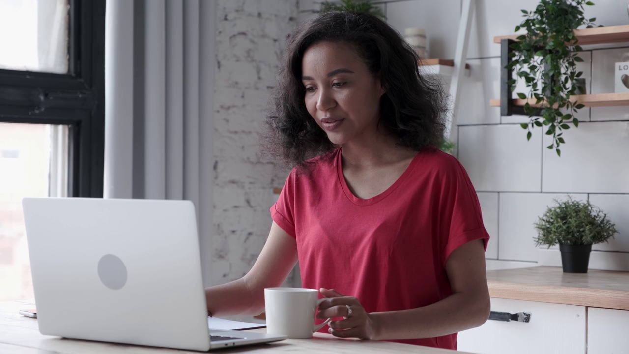 微笑的年轻非裔美国女性使用笔记本电脑并在笔记本上做笔记视频下载
