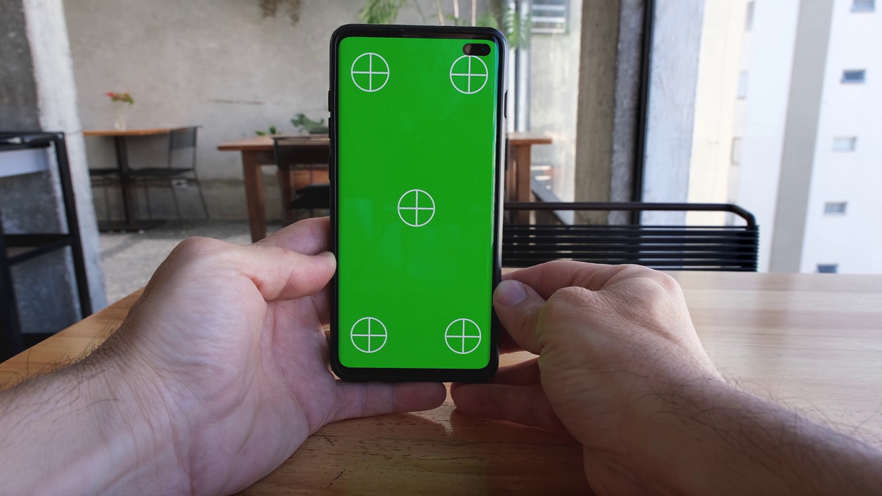 男性手持智能手机垂直观看绿色屏幕和标记。视频下载