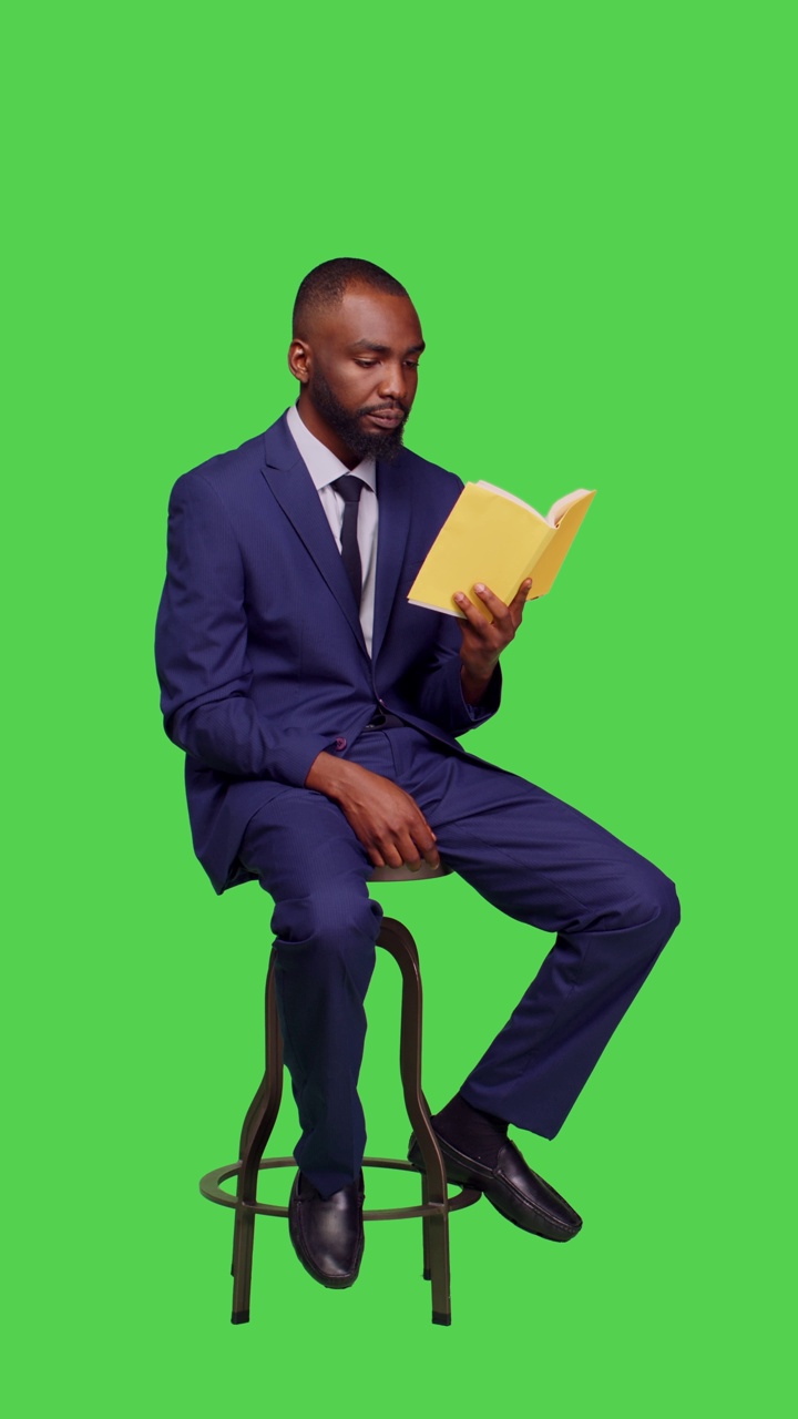 垂直视频:一个非裔美国人坐在椅子上读小说的侧视图视频下载