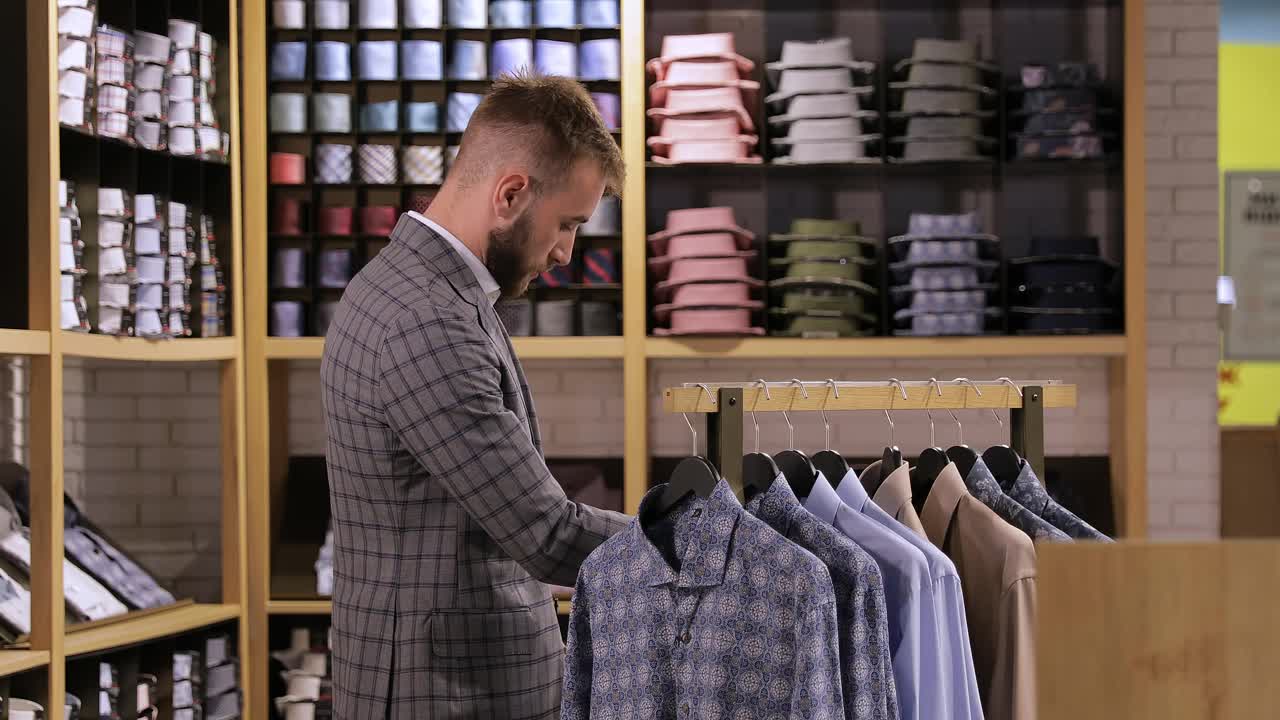 一个商人在商店里挑选了一件男衬衫，把它从衣架上拿下来。视频下载