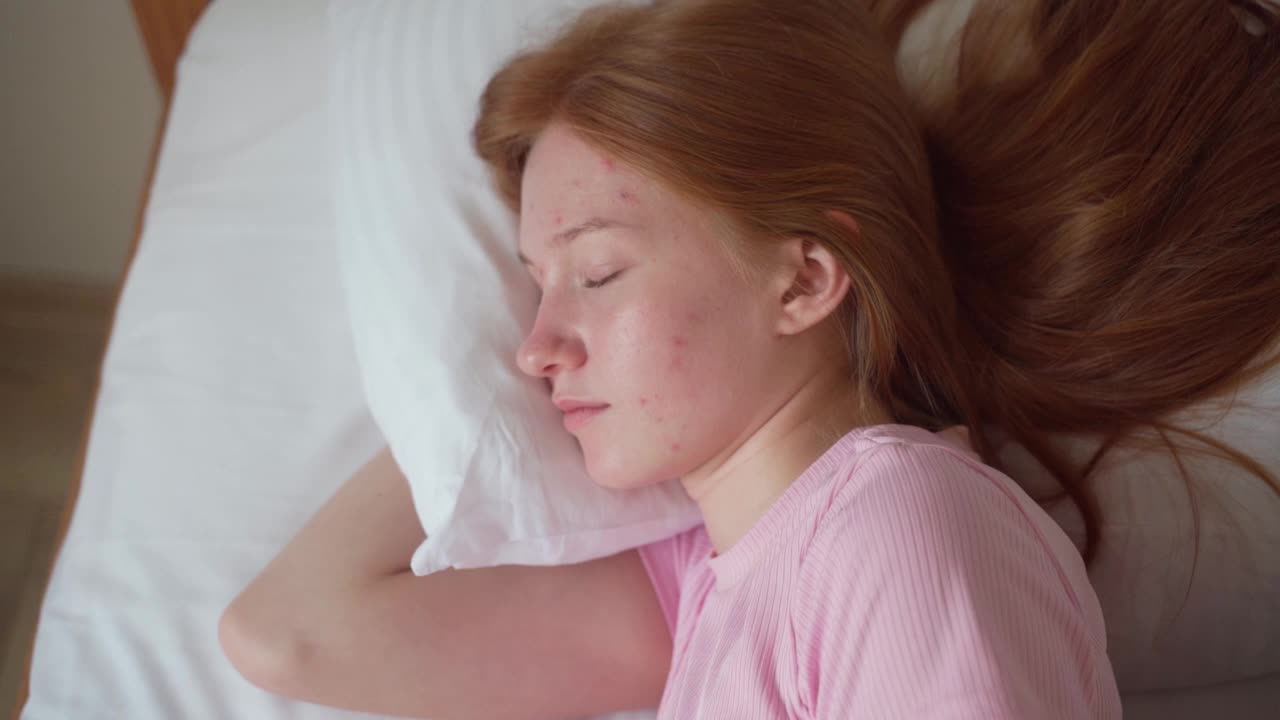 快乐困倦的年轻红头发十几岁的女孩醒来躺在舒适的白色床上。积极漂亮的姜色少年在舒适的卧室里享受着清晨的美好。新鲜的懒人在家里健康地睡了一觉后醒来。视频素材