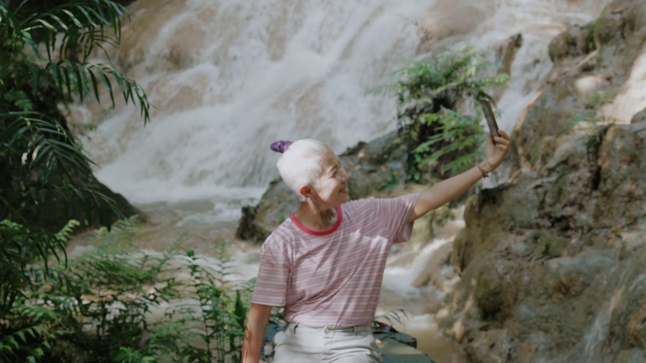 高级成年潮游客在宁静森林的瀑布享受独自旅行。视频下载