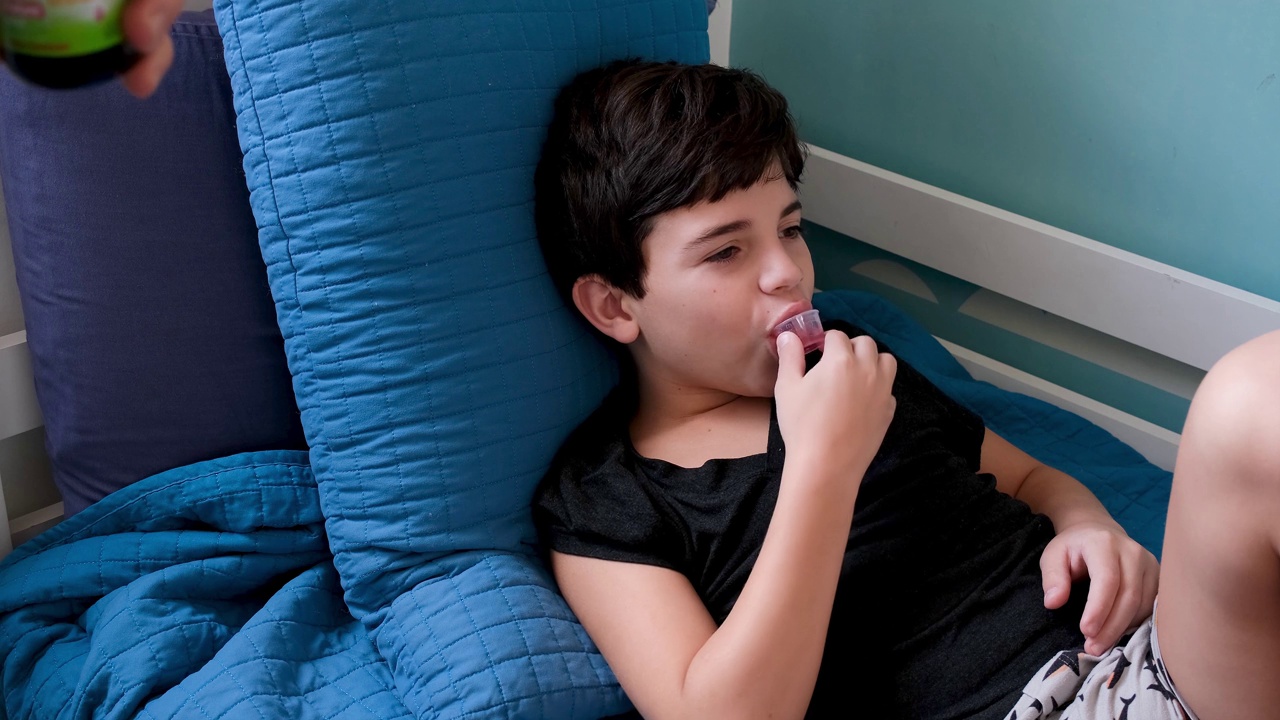 9岁的孩子患流感躺在床上，从他的父亲那里得到糖浆和慈爱。视频下载