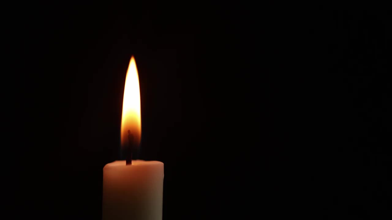 特写镜头。一支白色的蜡烛在燃烧。橙色的火焰。风来回吹。黑暗背景夜视频下载