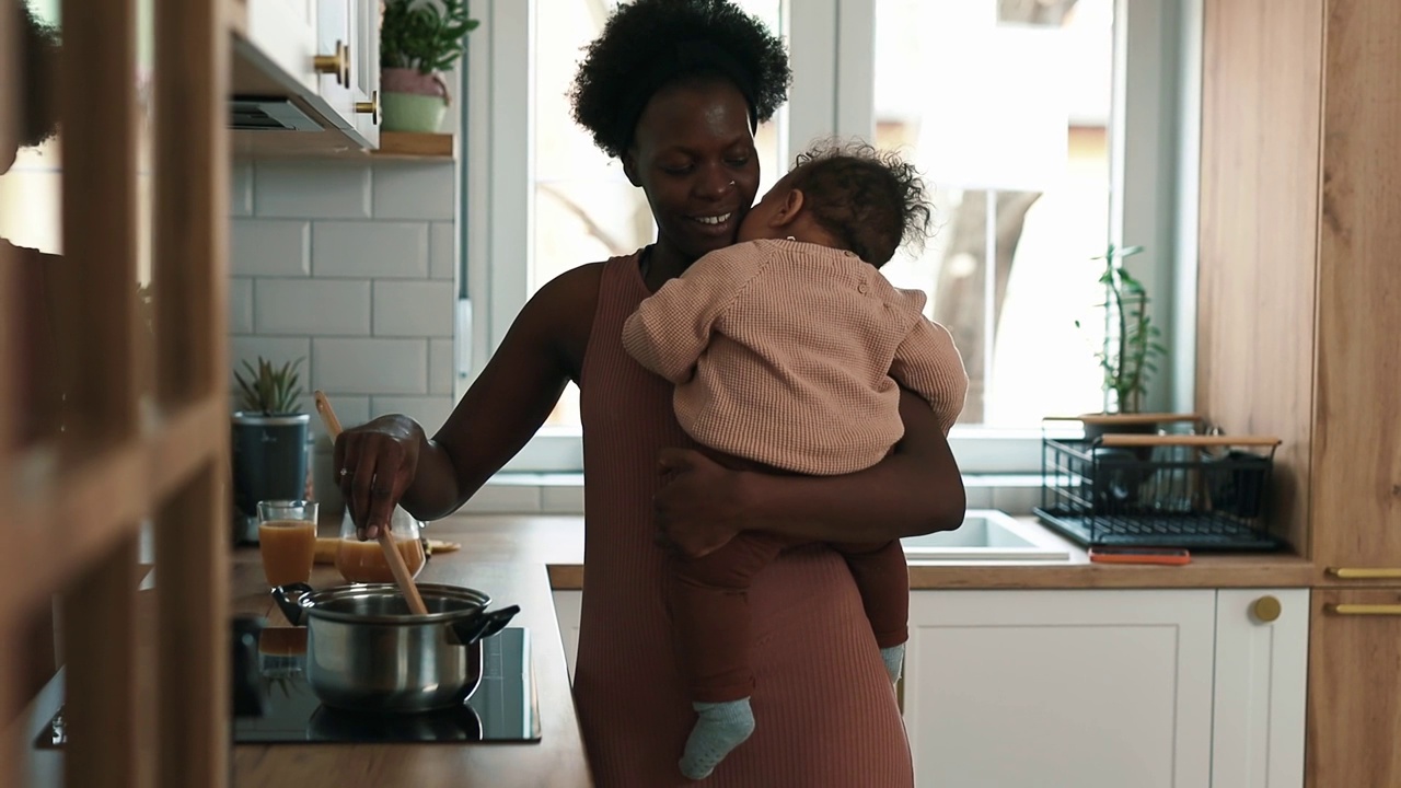 母亲抱着一个男婴在家里的厨房里做饭视频下载
