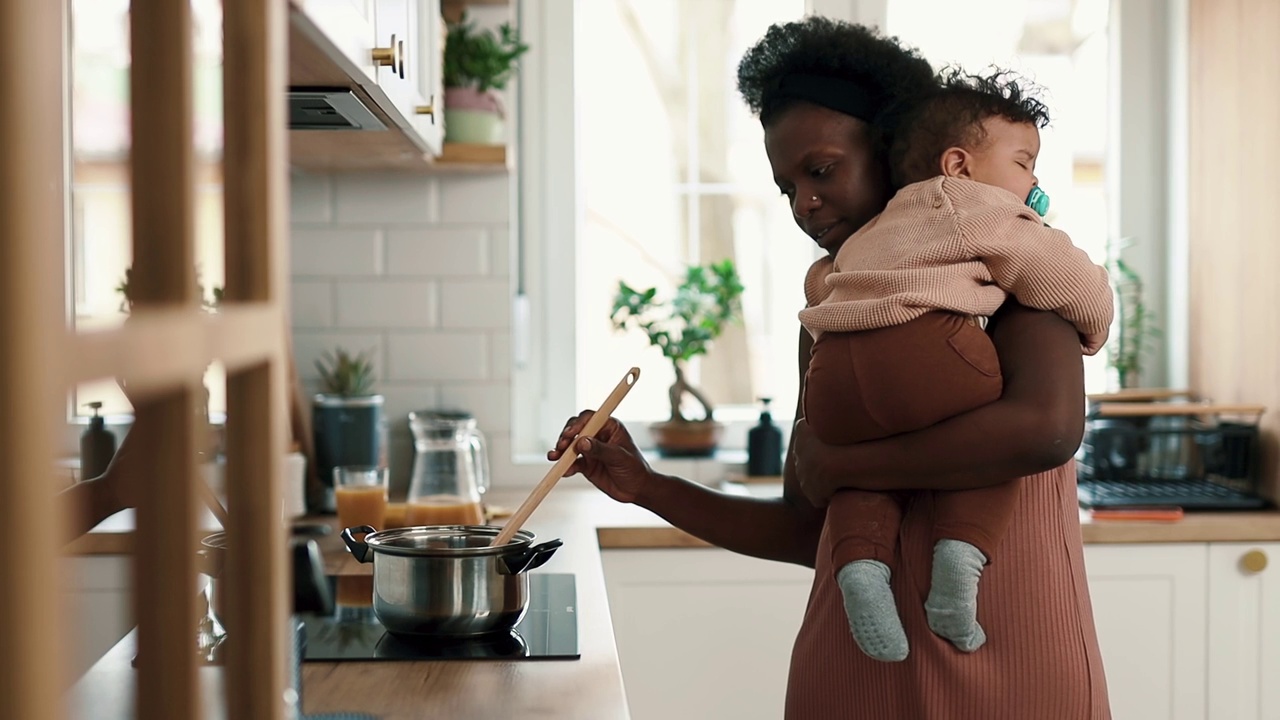 母亲抱着一个男婴在家里的厨房里做饭视频下载
