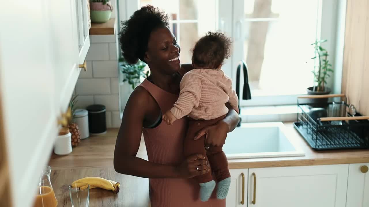 妈妈抱着孩子在厨房里倒鲜榨果汁视频下载