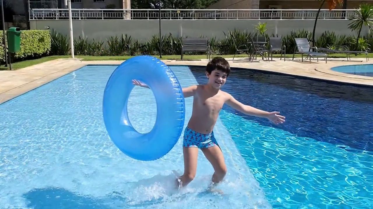 9岁的巴西小男孩抱着浮标，在泳池里滑稽地走着跳着。视频下载