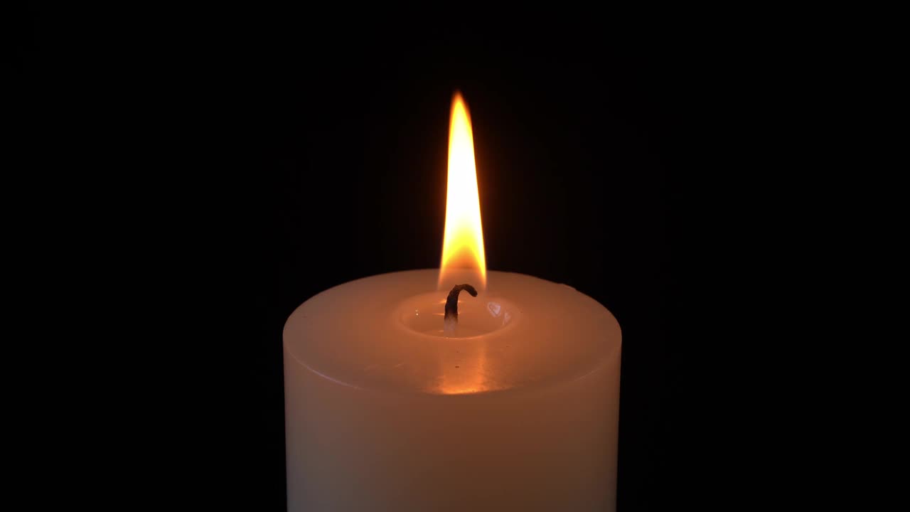 点燃的蜡烛孤立在空旷的深黑色背景上视频下载