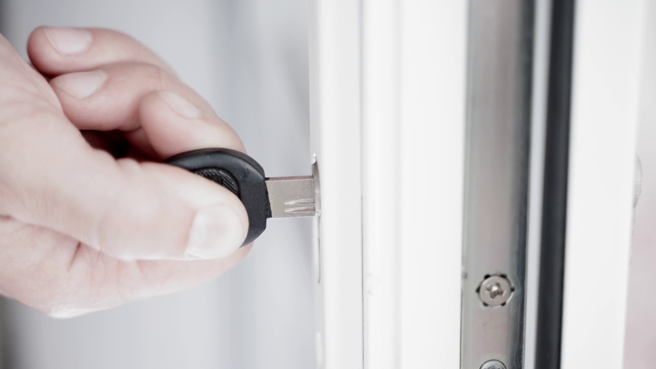 检查塑料门上的锁是否运转正常。一只手将一把带孔的钥匙插入锁眼，特写视频素材
