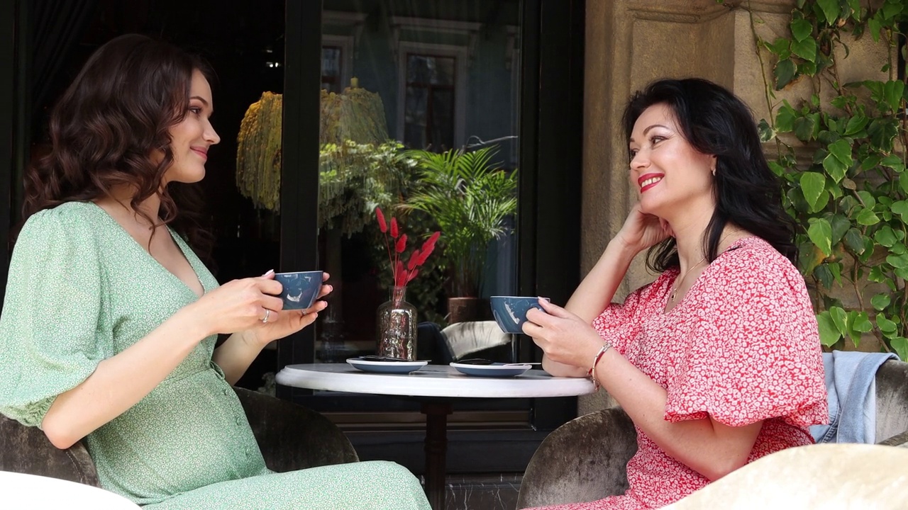 一个怀孕的女孩和一个女人在夏天的咖啡馆吃午饭，喝热咖啡。母女俩在咖啡馆吃饭。母亲节，4K分辨率视频下载