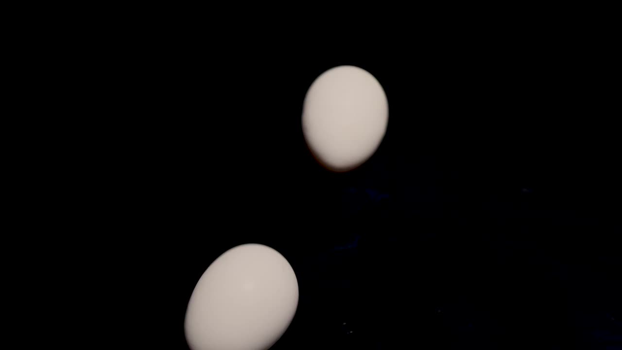 两个蛋清在黑色背景上旋转。烹饪材料。蛋清和蛋黄。两个复活节彩蛋。动物蛋白是有益的。视频素材