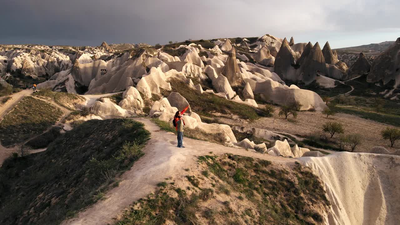 日落时分在卡帕多西亚徒步旅行的游客。站在卡帕多西亚自然保护区玫瑰谷的山顶上观看壮丽的景色。视频下载