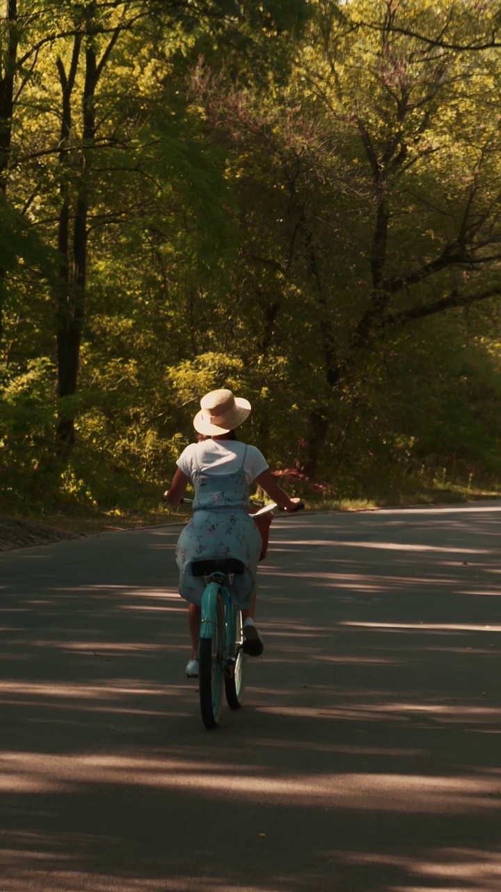 一个女人骑着复古的老式自行车在绿色的夏日公园里移动。垂直视频视频下载